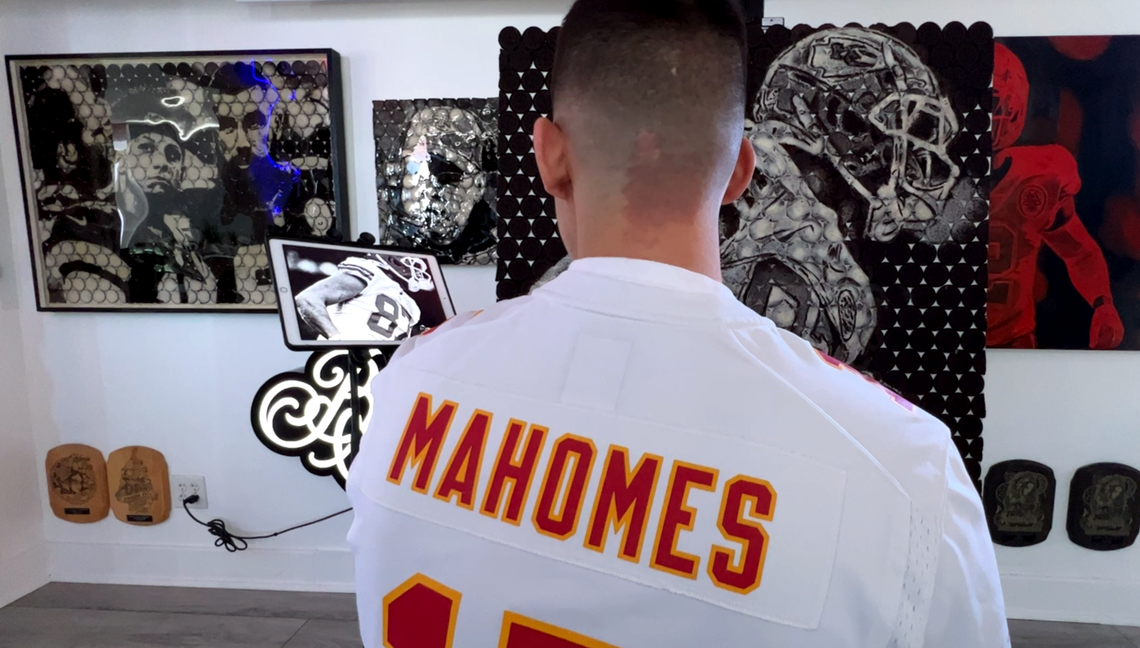 Artist Gabe Uvario, a faithful Kansas City Chiefs fan, wears a Patrick Mahomes jersey while studying a photograph of Travis Kelce as he finishes artwork of the tight end made from Oreo cookies.