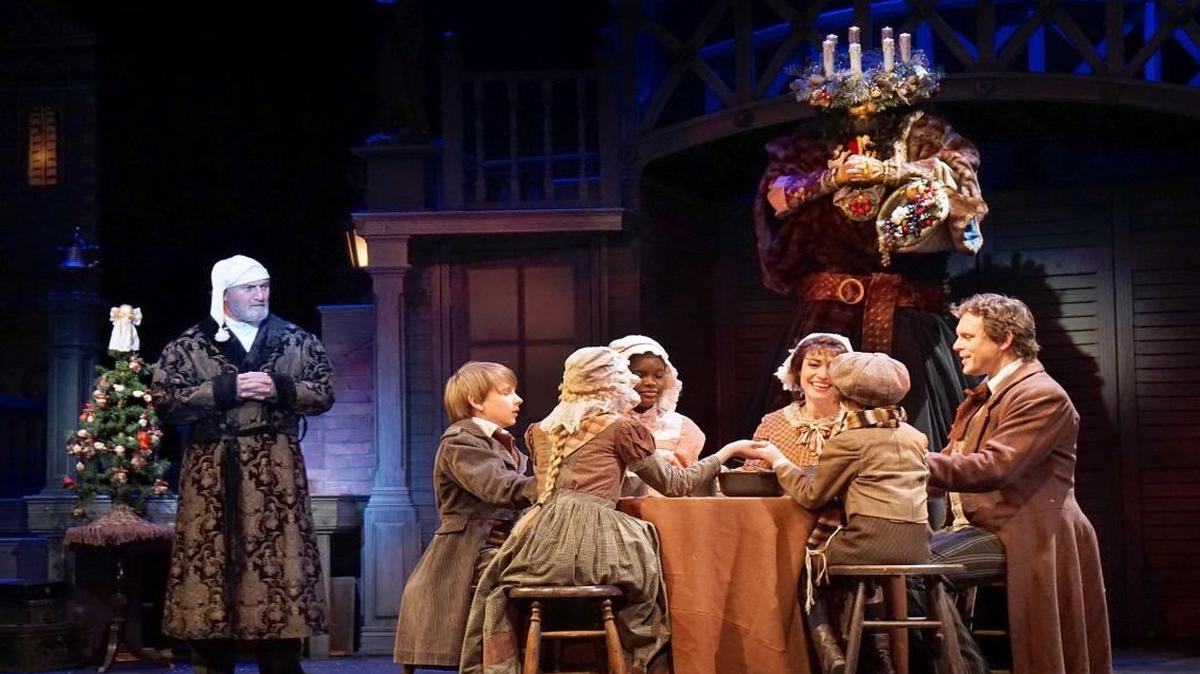 Thanks to the towering Ghost of Christmas Present, Ebenezer Scrooge (Gary Neal Johnson) sees the Cratchit family enjoying Christmas in spite of him.