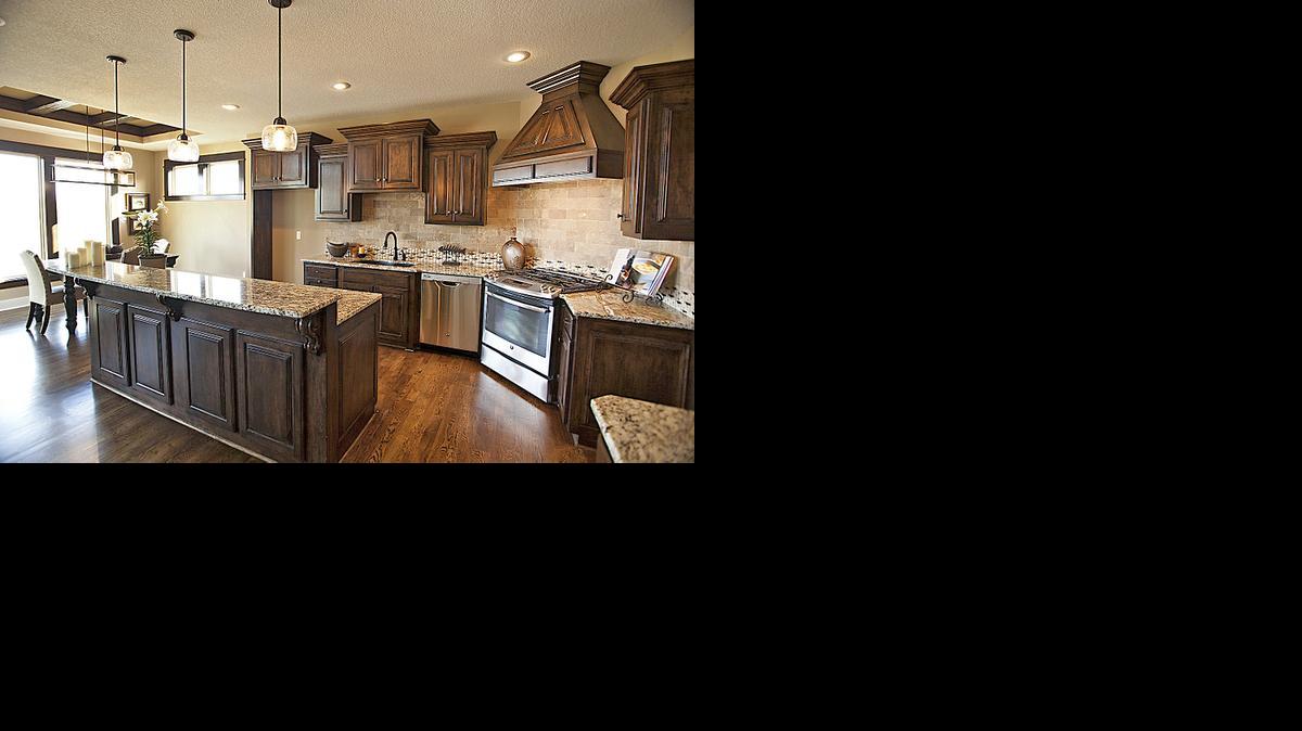 
The kitchen of HeatherGlen’s furnished model home features custom-raised panel maple cabinets, soft-close drawers, granite counter tops, charging center, vaulted beam ceiling, stainless steel appliances and an island with pull-out microwave drawer. 
