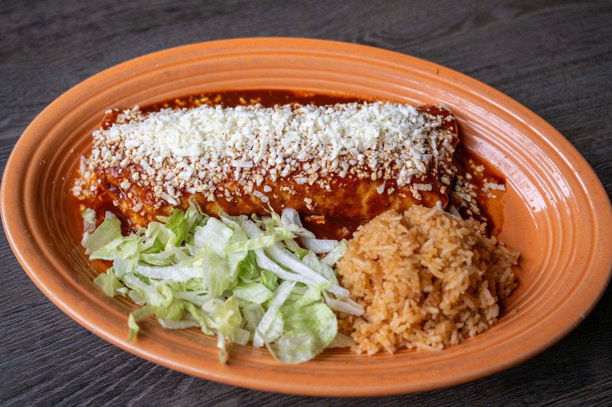 The enchilada burrito, featuring pork, chicken, or ground beef options, is wrapped in a flour tortilla with refried beans, topped with house-made enchilada sauce and queso fresco and served with a side of rice and lettuce at Rudy’s Tenampa Taqueria.