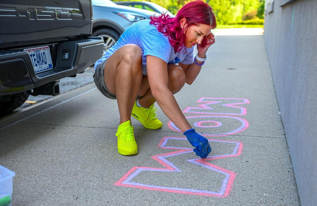 April Shaver uses chalk to write “Mom” on the sidewalk outside the Kindred Hospital Northland room where her mother, Gwen Starkey, 59, is a COVID-19 patient.