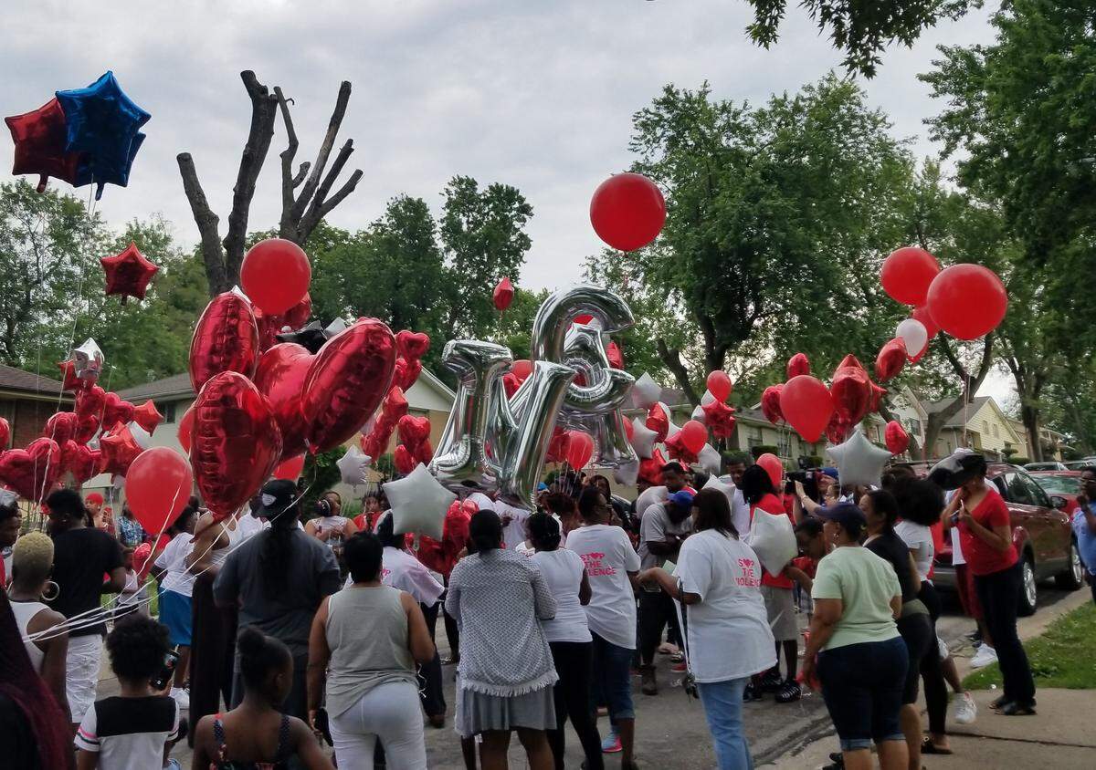 One balloon starts slipping away just before the crowd releases the balloons at a vigil for three men killed last year.