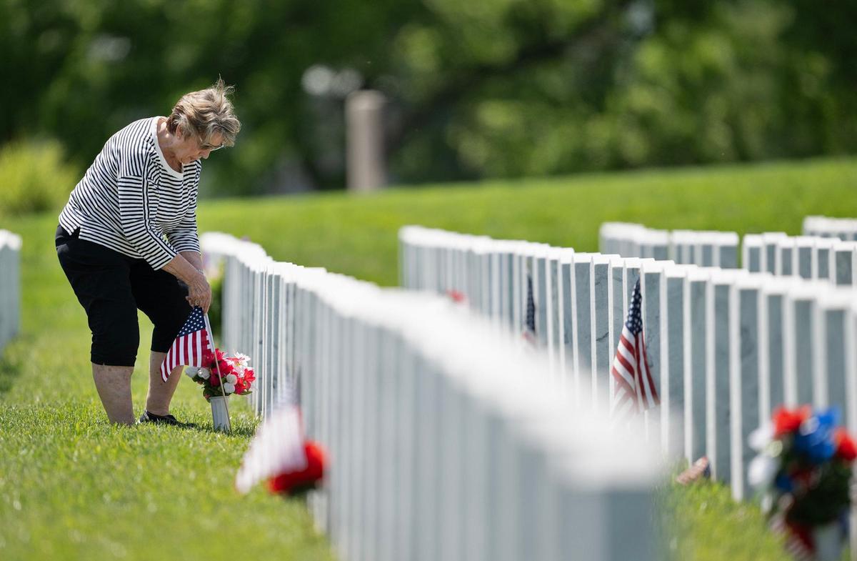 Vicki Sims of Leawood adds flowers and a flag to the grave of her father, Bill Browning, a U.S. Army veteran, during a visit Thursday, May 23, 2024, to Leavenworth National Cemetery ahead of the Memorial Day holiday. Sims paid her respects with her husband, Bruce Sims.
