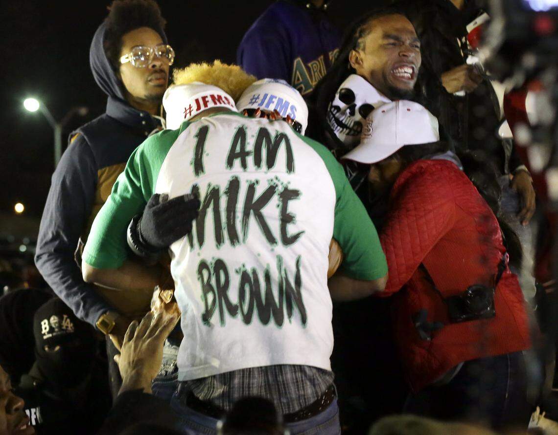 Lesley McSpadden, the mother of Michael Brown, second from left standing on the top of a car, hugs an unidentified man, wearing an I am Mike Brown shirt, as she listens to the announcement of the grand jury decision Monday, Nov. 24, 2014, in Ferguson, Mo. A grand jury has decided not to indict Ferguson police officer Darren Wilson in the death of Michael Brown, the unarmed, black 18-year-old whose fatal shooting sparked sometimes violent protests. (AP Photo/Charlie Riedel)