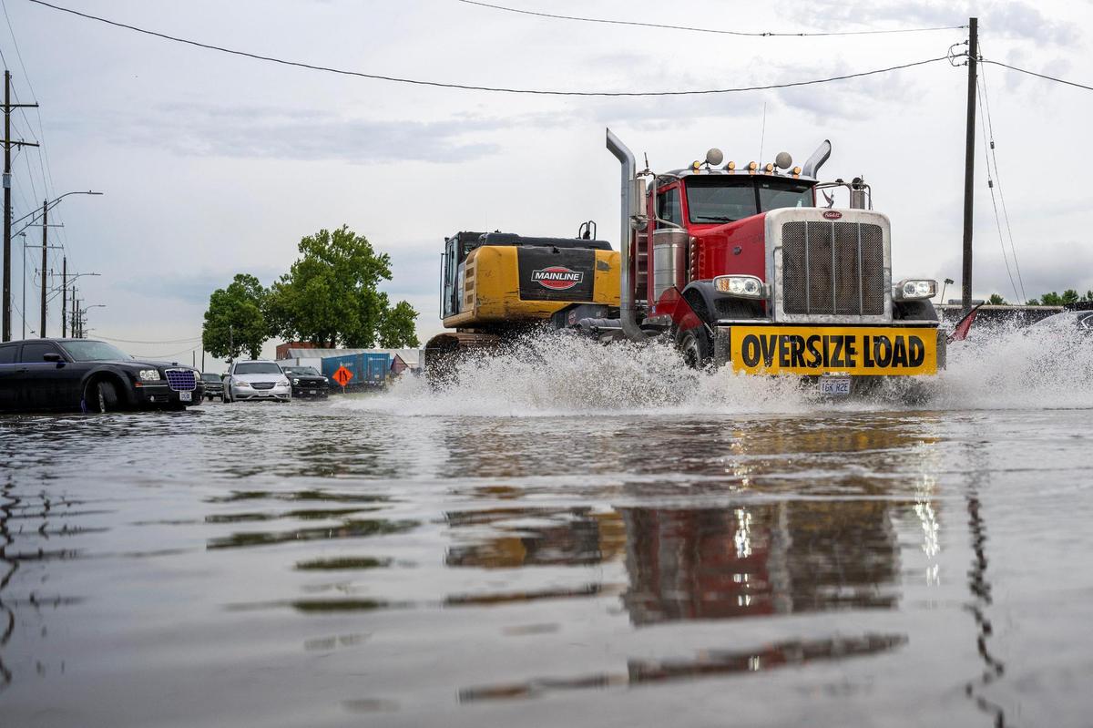 A truck marked for oversized loads drives through floodwaters along Gardner Avenue on Thursday, July 17, 2025, in Kansas City. Flash flooding from heavy overnight rain left portions of the road partially submerged.