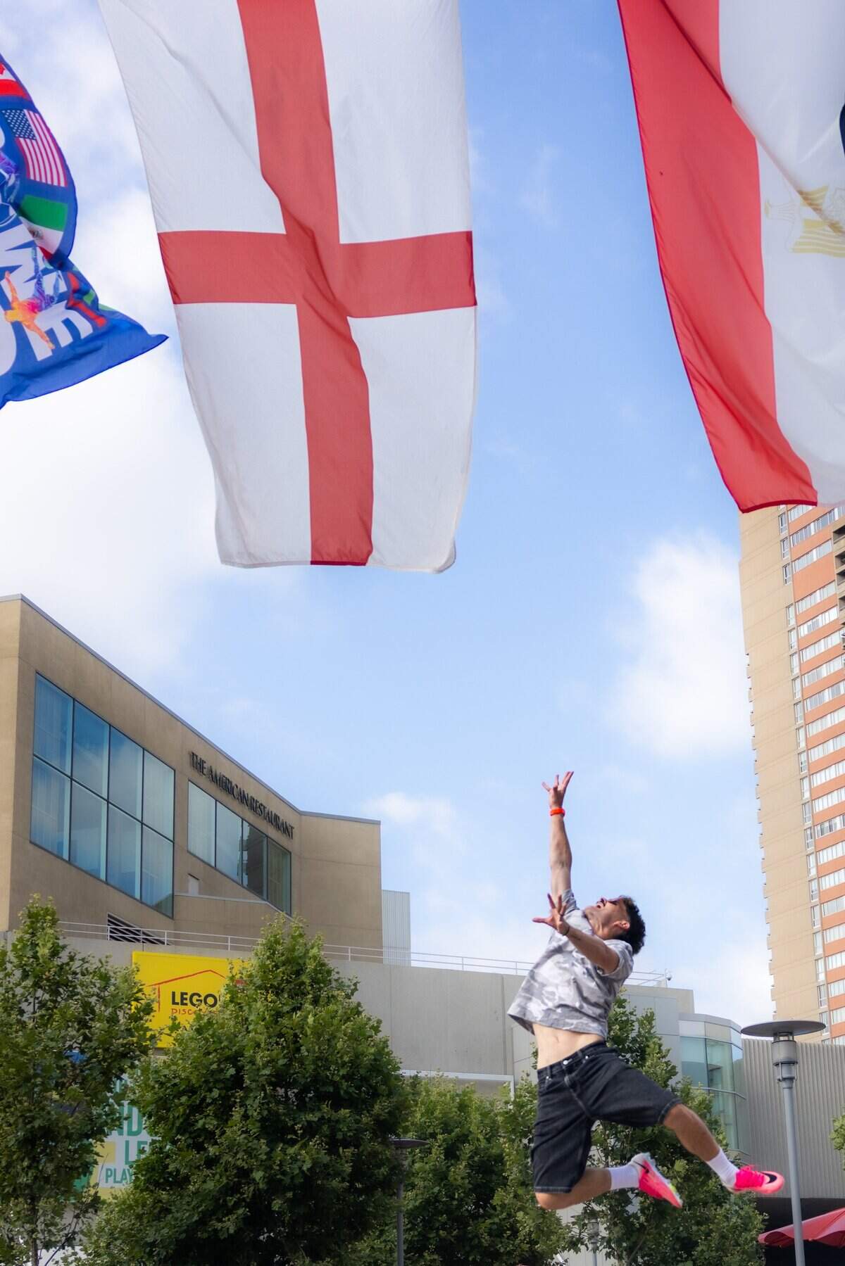 Oliver Wright jumps to try and touch the flag of England at Crown Center on Sunday, June 28, 2026. Also known online as “Side Quest Dad,” he’s a British content creator who has lived in Kansas City for the past 15 years and shares everyday adventures with his followers through social media. He recently gained local attention after a viral video warning World Cup visitors about Midwest summer weather.