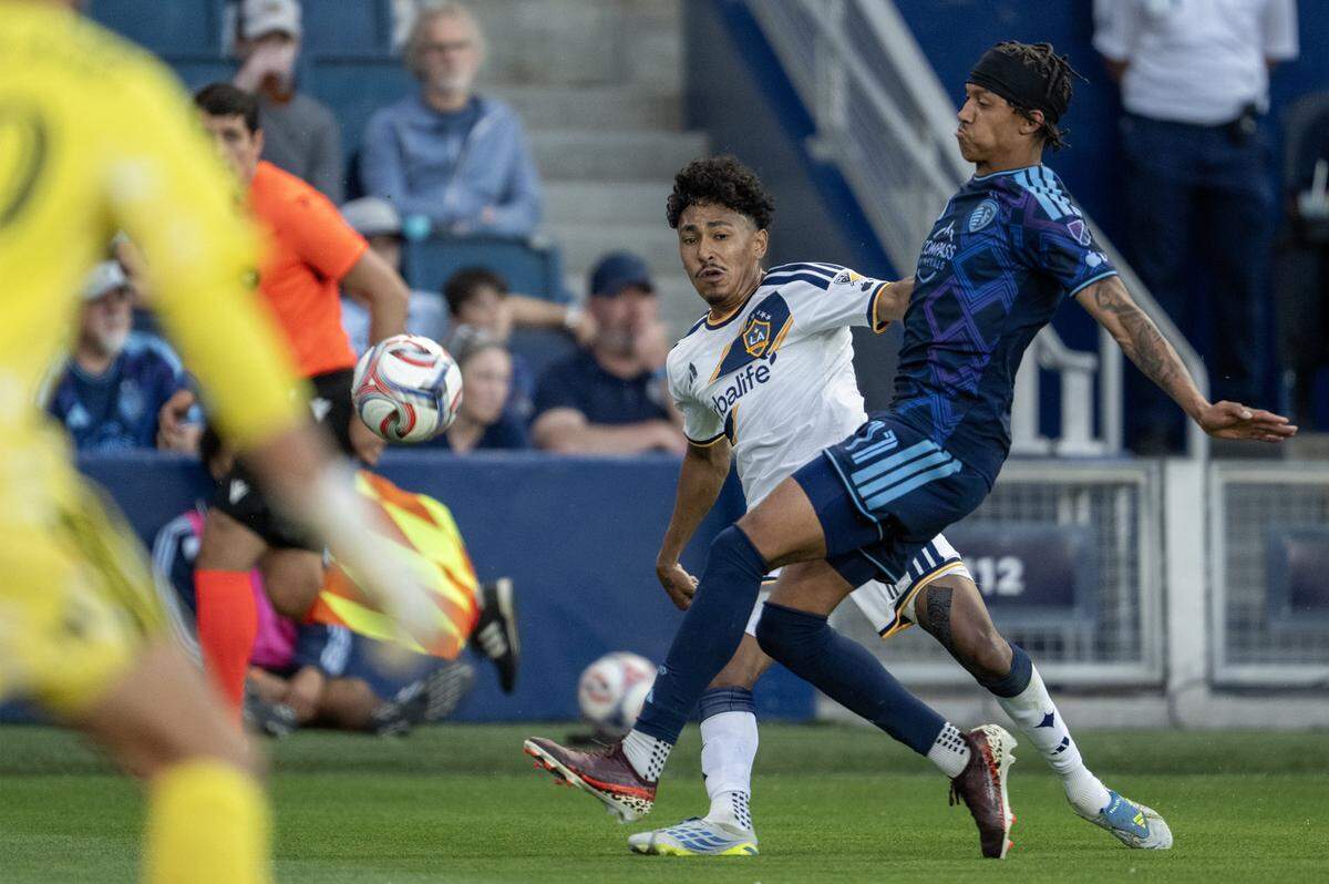 LA Galaxy defender Mauricio Cuevas (19) and Sporting Kansas City forward Calvin Harris (11) go after the ball during the first half at Sporting Park on Wednesday, May 13, 2026, 2026, in Kansas City, Kansas,