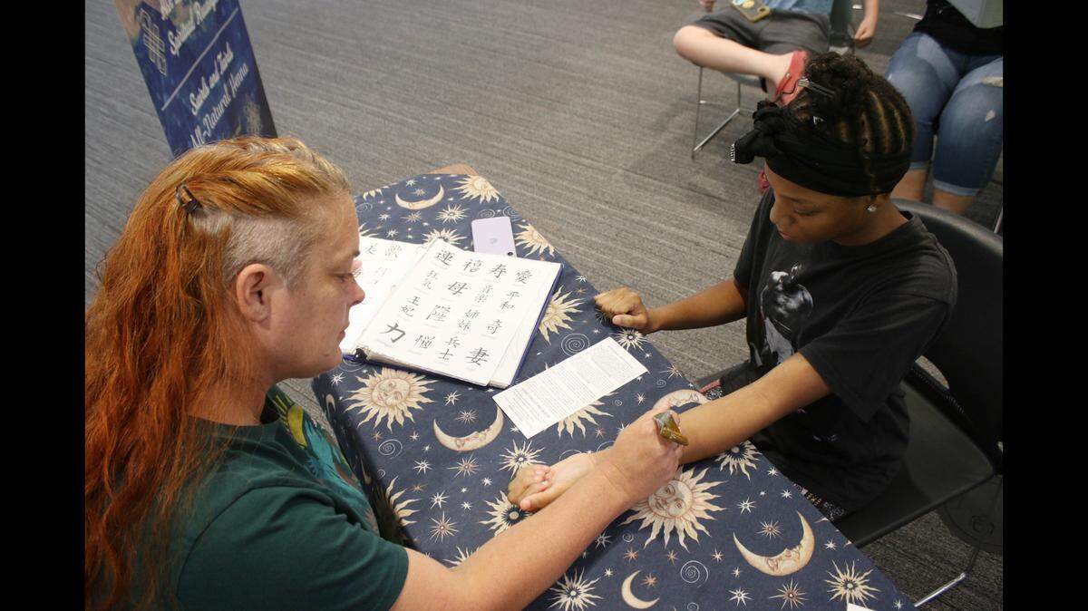 Becky Hicks of Swirls and Twirls Body Art draws a henna tattoo on 12-year-old Lee’s Summit resident Da’Mya Hardin during a program at the Lee’s Summit branch of the Mid-Continent Public Library.