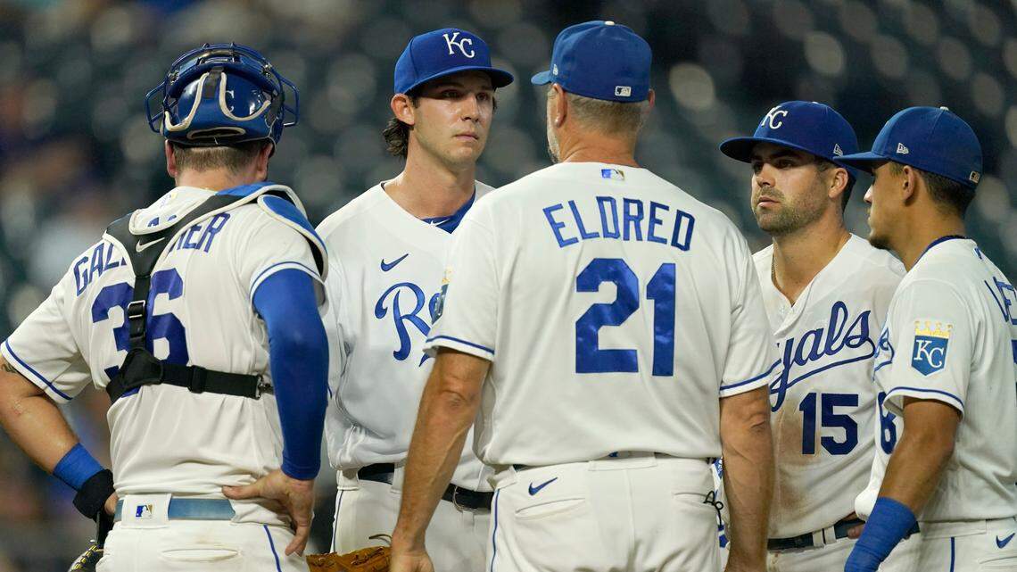 Kansas City Royals pitching coach Cal Eldred (21) talks to starting pitcher Daniel Lynch, second from left, during the fourth inning of a baseball game against the Cleveland Indians Wednesday, Sept. 29, 2021, in Kansas City, Mo. (AP Photo/Charlie Riedel)