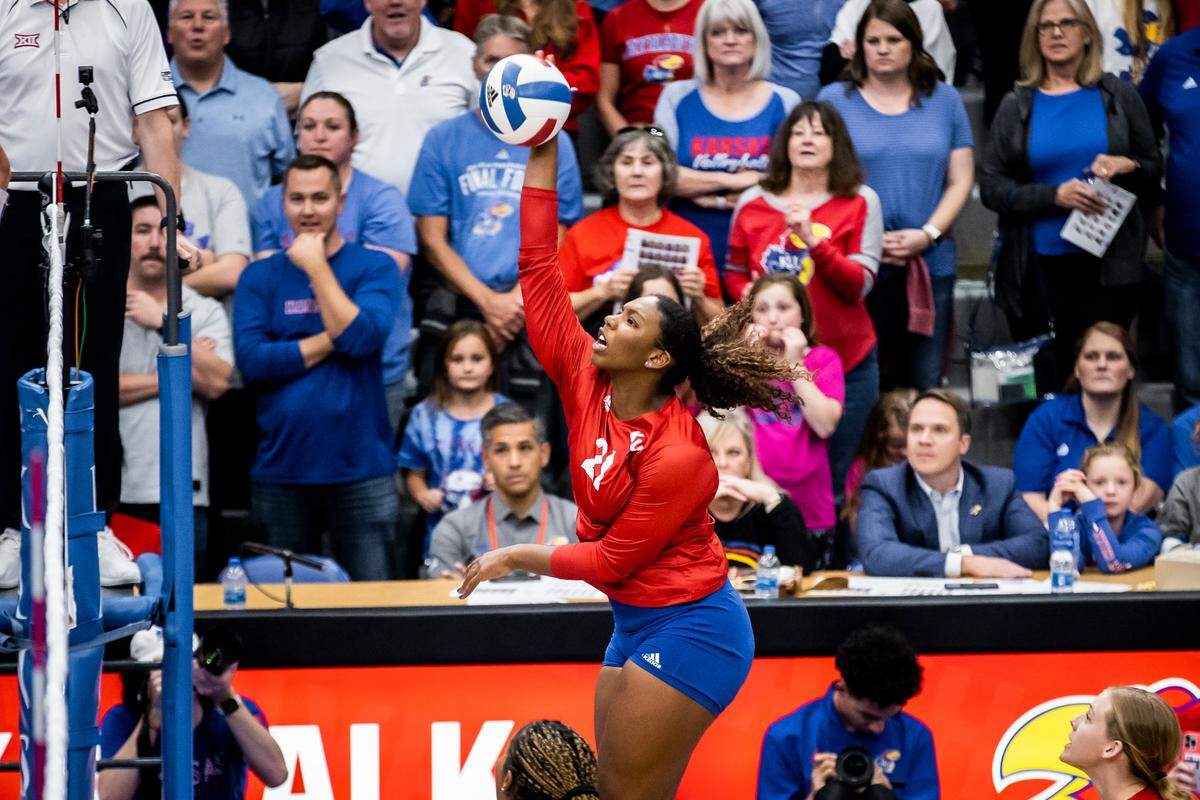 London Davis (21) of the Kansas volleyball team hits the ball while athletic director Travis Goff (seated) looks on during a match between KU and K-State at Horejsi Family Athletics Center in Lawrence, Kan.