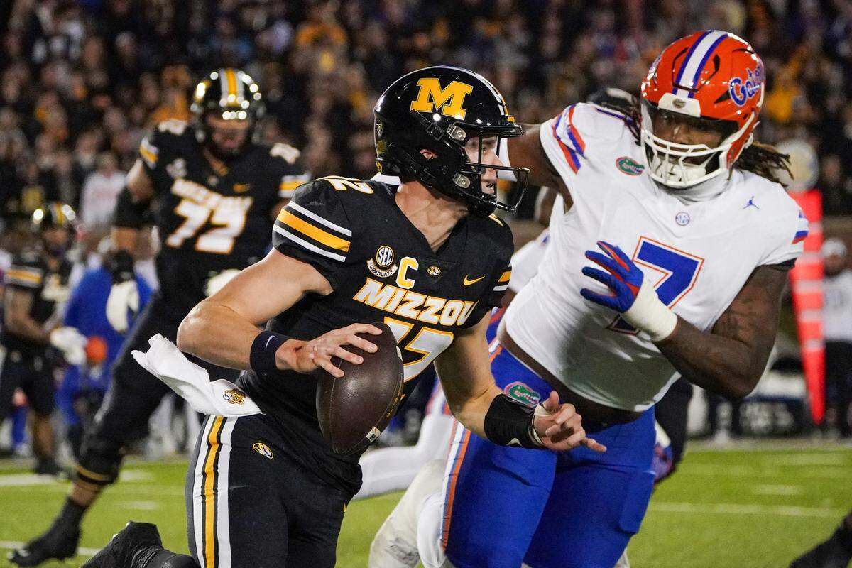 Missouri Tigers quarterback Brady Cook (No. 12) runs the ball as Florida Gators defensive lineman Chris McClellan defends during Saturday night’s game at Faurot Field at Memorial Stadium in Columbia. Mo.