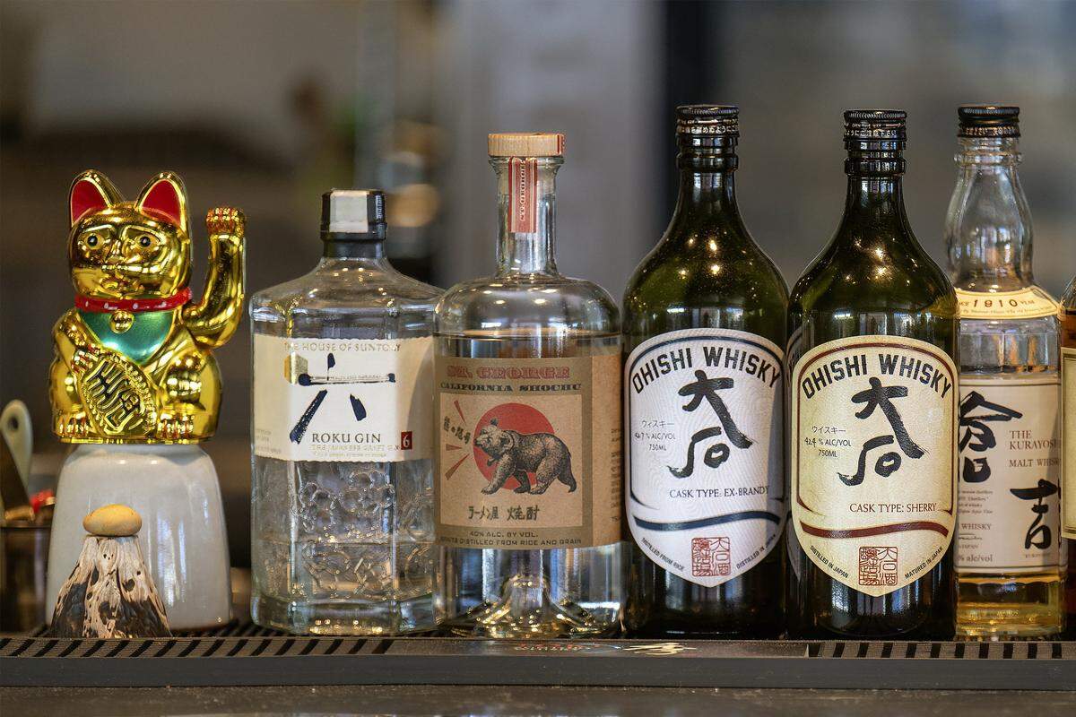 A gold maneki-neko (beckoning cat), a Japanese good-luck charm, sits beside a bottle of Roku Gin and other Japanese spirits at Anjin, a Japanese Izakaya-style restaurant, on Monday, March 16, 2026, in Kansas City.