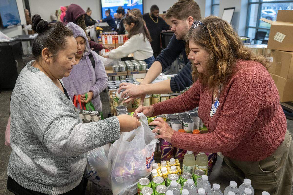 Jacob Glascow, second from right, Tina Alewel, right, help clients including Jan Inth, left, of Kansas City, select groceries during Harvester's monthly food distribution at Jackson County Public Health in Lee's Summit on Wednesday, November 19, 2025. The distribution, which drew a large crowd, is part of ongoing efforts to combat food insecurity in the community by providing residents with essential food items.
