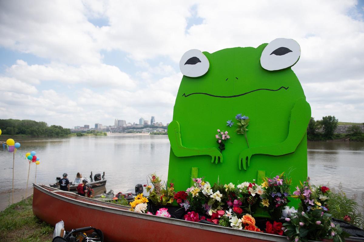 A canoe decorated with a large wooden frog and variety of plastic flowers awaits launch before the Kawsmouth River Carnival boat parade.