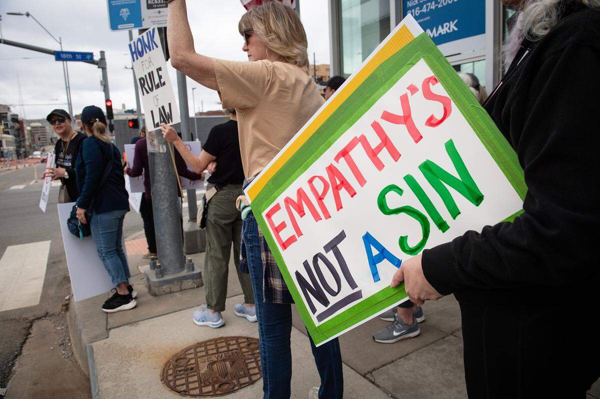 Demonstrators hold signs during a pro-democracy march that took aim at the Trump administration’s policies Saturday, March 29, 2025 in downtown Kansas City.