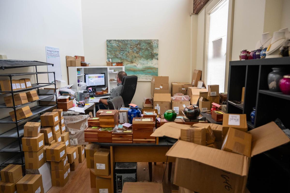 Jarrod Hammond, owner of Heartland Pet Aquamation, 1414 Wyamong St. sits at his computer at a desk surrounded by supplies, urns and cedar boxes filled with the cremated remains of pets.