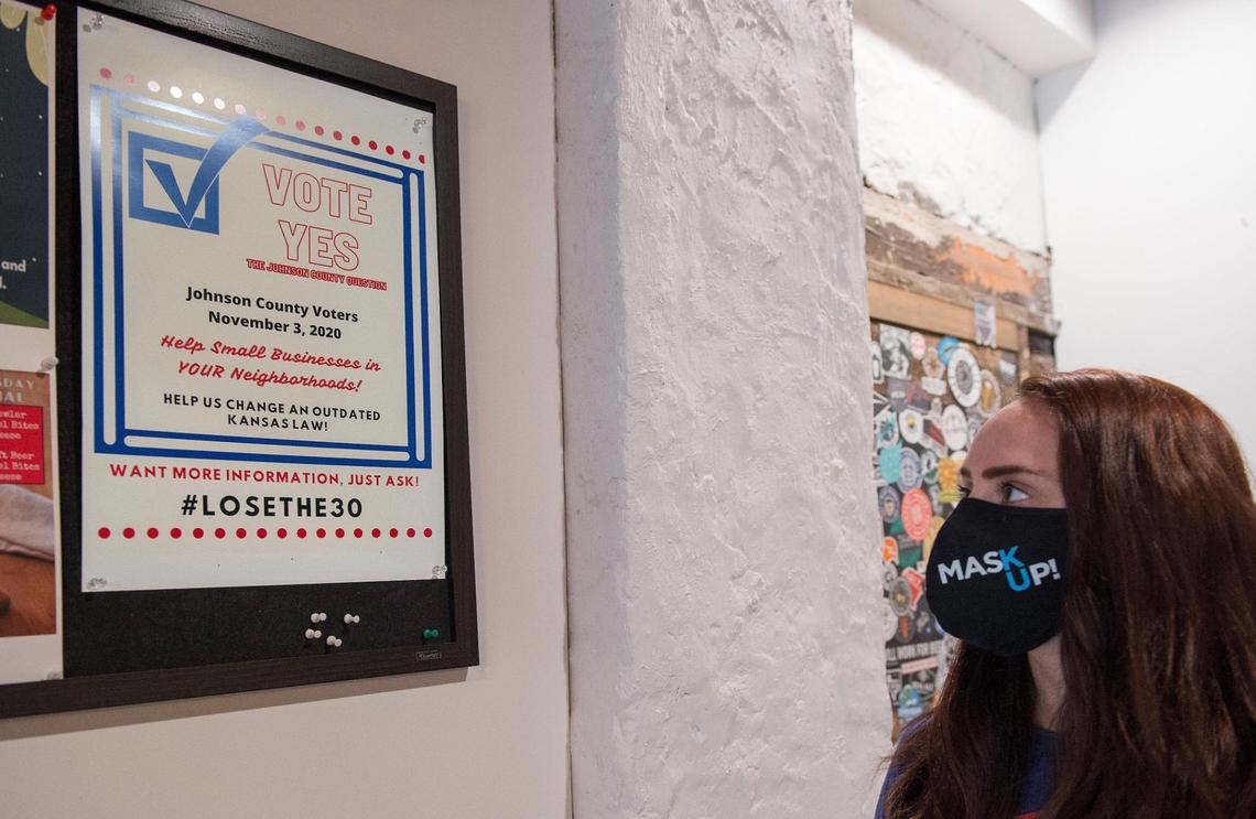 Christie Merandino, operations manager of Transport Brewery in Shawnee, shows how bars are hanging signs to support a ballot initiative in November. Johnson County voters will be asked to repeal a law requiring bars to make a certain amount of sales from food. She says that has added an unnecessary burden on business owners. 