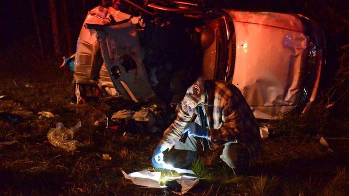 Hancock County, Miss., Coroner Jim Faulk searches through documents in an attempt to identify two victims from a Ford Explorer, background, who died in an accident on Saturday Dec. 13, 2014, on Interstate 10 in Hancock County, in Kilm, Miss. Four people were killed in the 11-vehicle accident.