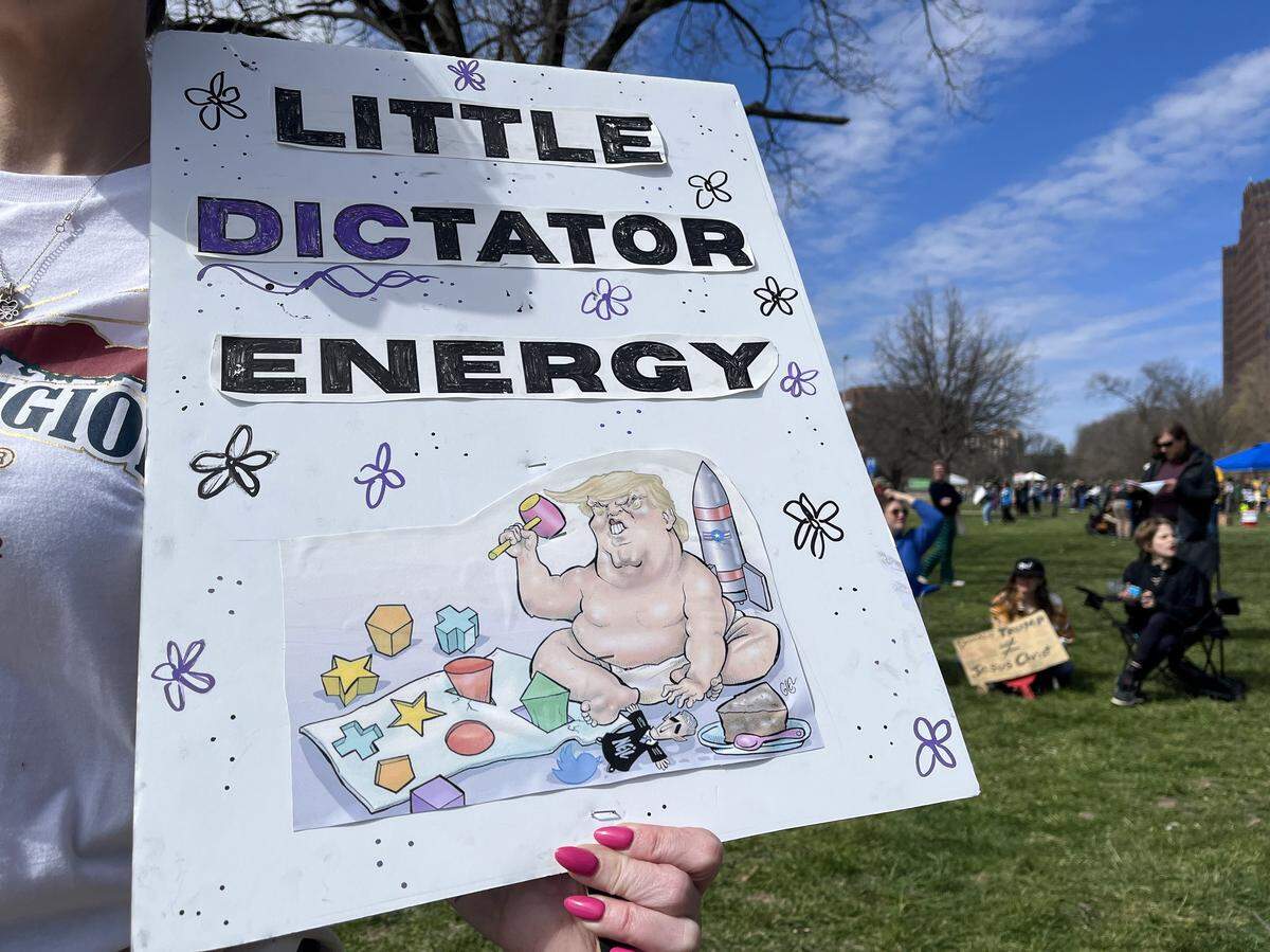 A protester holds up a sign in Mill Creek Park in Kansas City on Saturday, March 28, 2026, during a No Kings protest against the Trump administration.