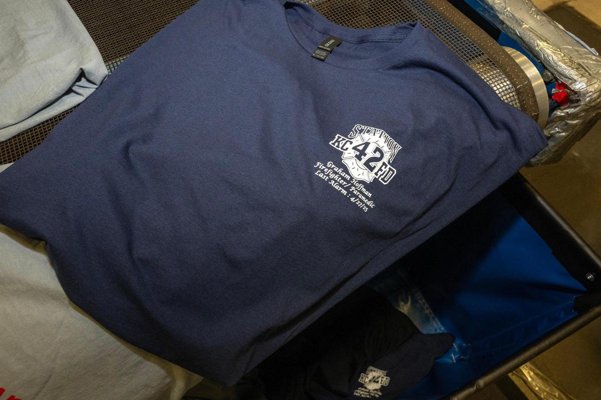 Memorial T-shirts honoring Kansas City Fire Department firefighter Graham Hoffman emerge from the dryer and are readied for distribution at E2 Embroidery & Screenprinting on Tuesday, May 13, 2025, in Kansas City. The shop has begun producing these shirts to honor Hoffman, who was fatally stabbed inside an ambulance.