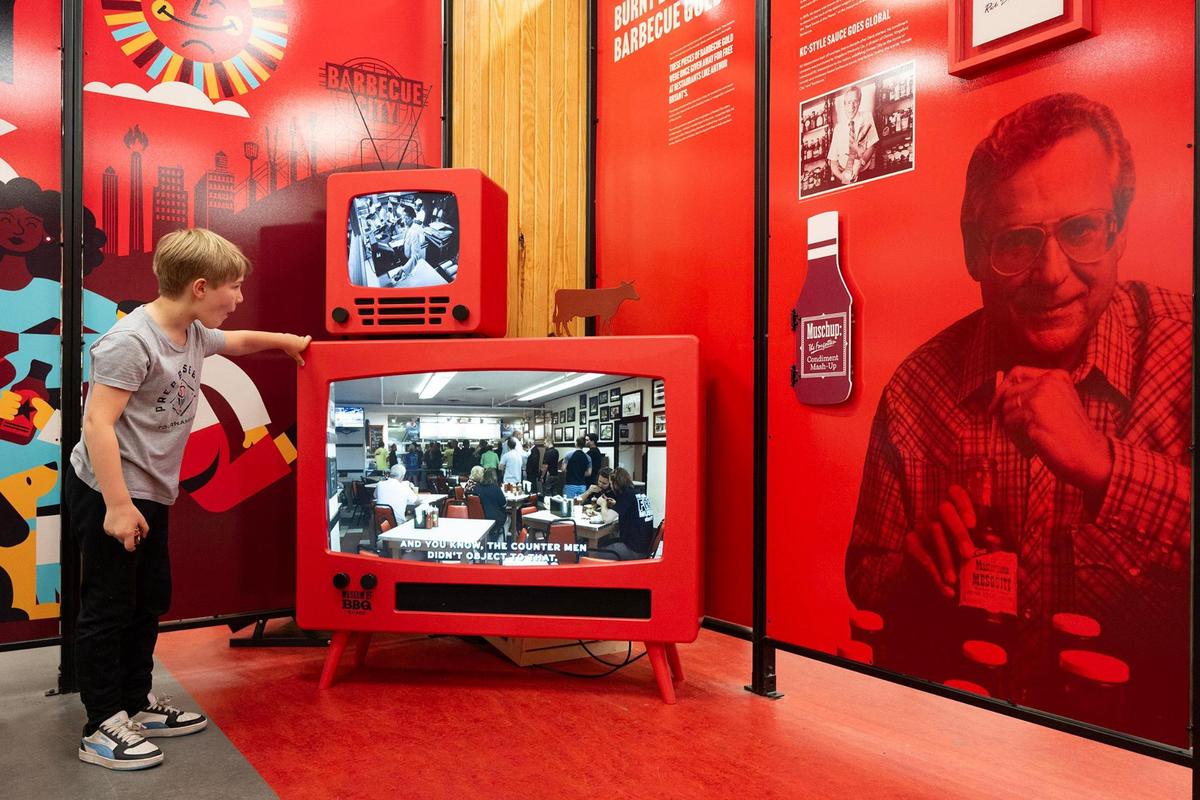 Teddy Van Dieren, 8, of Kansas City, watches a snippet of “Burnt Legend: The Story of Burnt Ends,” a documentary hosted by Jonathan Bender, who did the project in conjunction with Kansas City PBS. The exhibit is part of the new Museum of BBQ. KC Masterpiece founder Rich Davis is on the right.