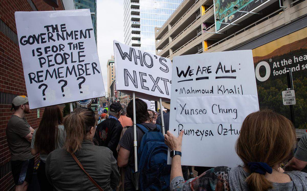 Demonstrators hold signs during a pro-democracy march that took aim at the Trump administration’s policies Saturday, March 29, 2025 in downtown Kansas City.