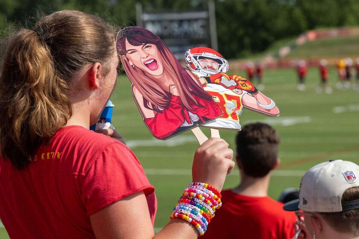 A young Chiefs fan wearing a wristful of friendship bracelets holds cardboard cutouts of Taylor Swift and Travis Kelce during practice at Chiefs training camp.