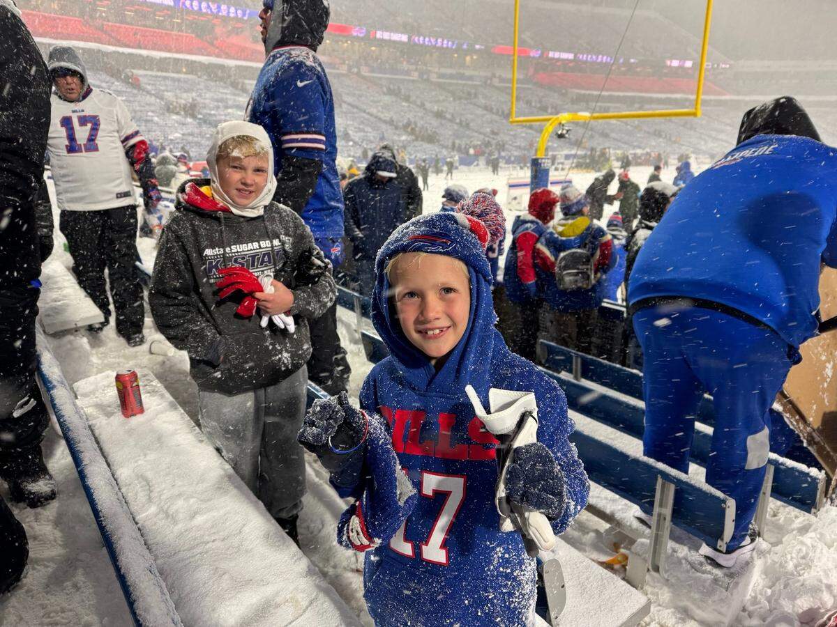 Asher Radzavicz shows off a glove from Bills quarterback Josh Allen while his brother, Andy Radzavicz, looks on behind him at a 2024 Buffalo Bills game.