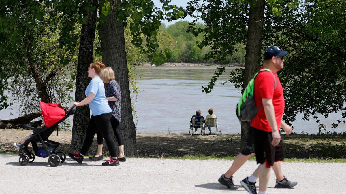A couple sits in lawn chairs as the Missouri River flows in front of them and walkers pass along a trail behind on a pleasant spring day Friday, May 1, 2020, in St. Charles, Mo. (AP Photo/Jeff Roberson)