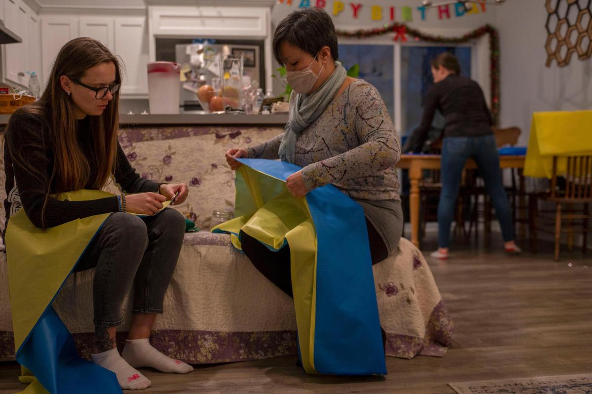 Olha Tkachenko, left, and Aiman Dvorak put pin needles on yellow and blue fabric to help make Ukrainian flags at Olga Potapenko’s home in Independence on Thursday, March 3, 2022. Potapenko is a wedding dress designer who has opened her home to help create Ukrainian flags as a thank you to anyone who has donated to support Ukraine.