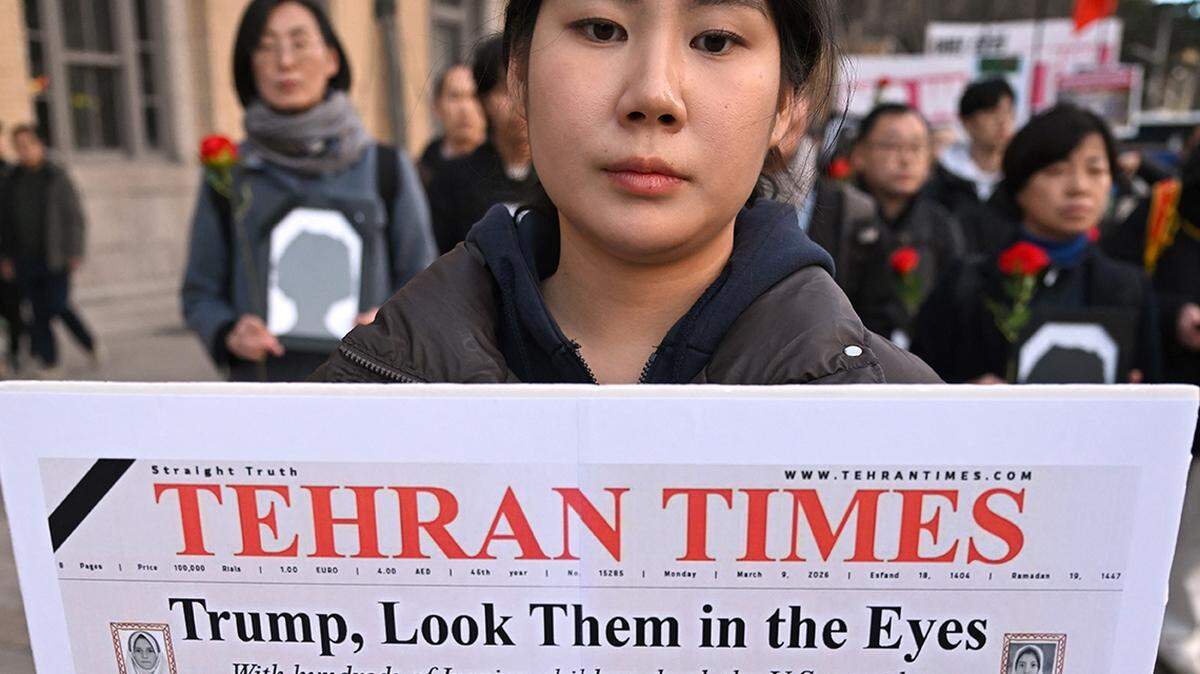 A woman carries a placard showing the front page of the Tehran Times following a deadly American strike on an elementary school in Minab, Iran.