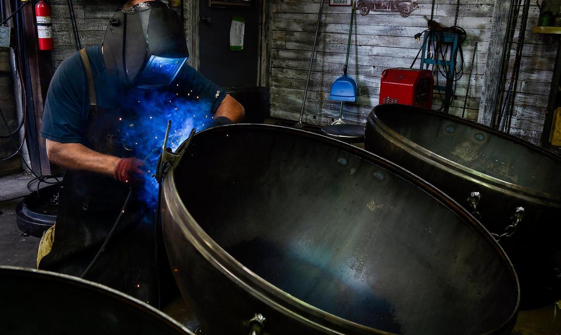 Brad Easley left his job as an electrician last year to make handcrafted fire pits full time at his business, Rough & Rigid. When the coronavirus hit, Easley said it was scary. But business has only grown. Easley makes the fire pits at his Basehor shop. Here, he welds on nameplates.