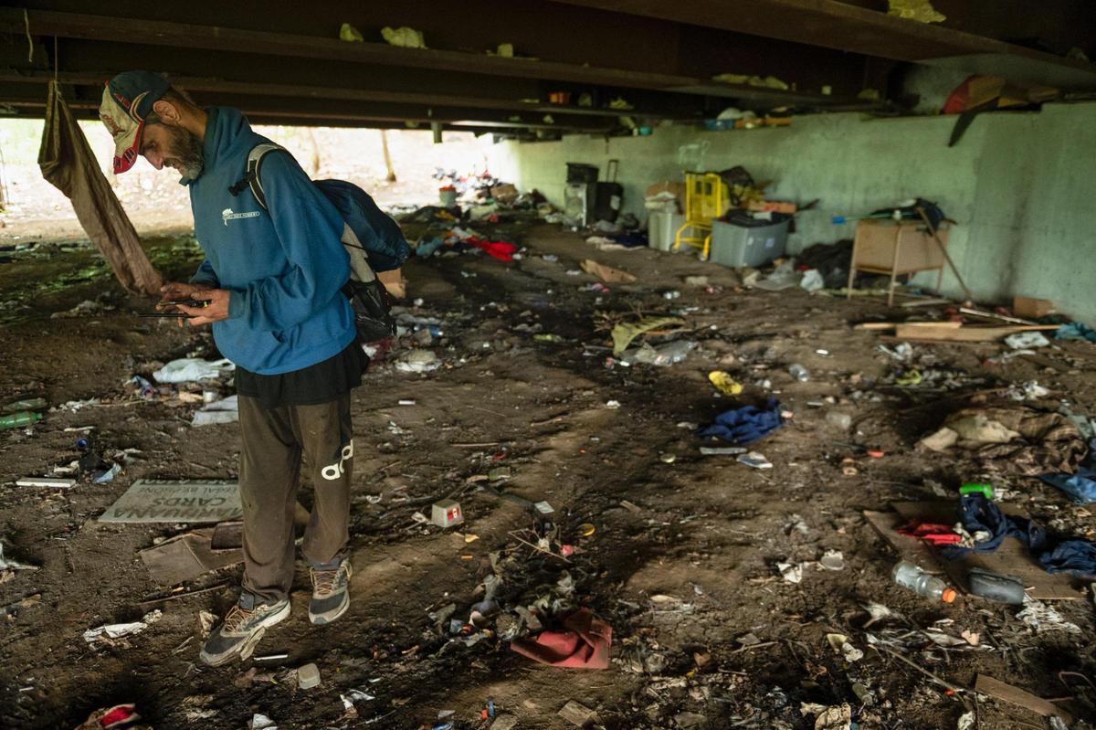 Ken Simard checks the battery life on his phone under a bridge where he lives in Kansas City. Simard relied on close friends to help him nurse his bullet wounds after he was shot in January 2023.