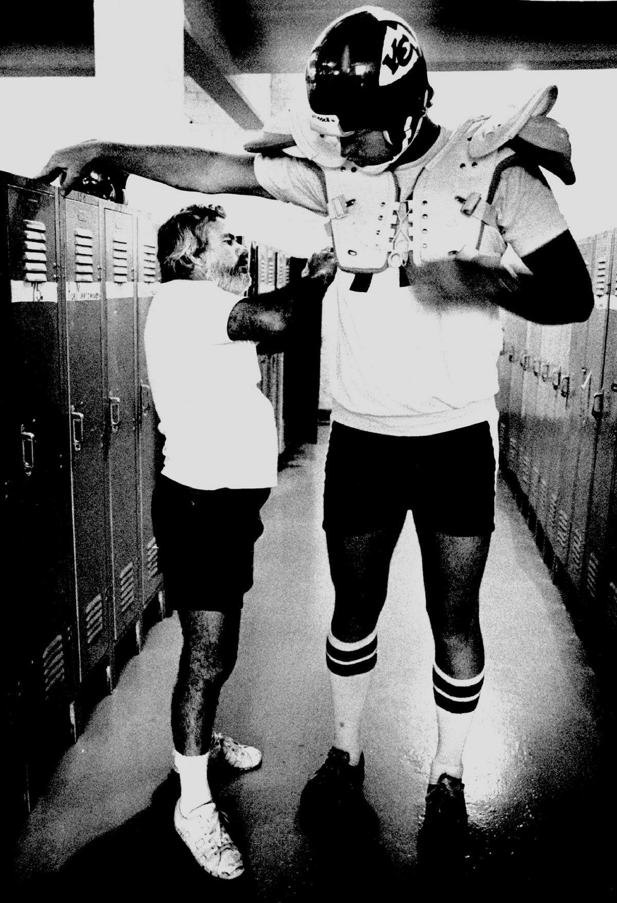 Kansas City Chiefs’ equipment manager Bobby Yarborough helps rookie Dale Markham with his shoulder pads in 1980.
