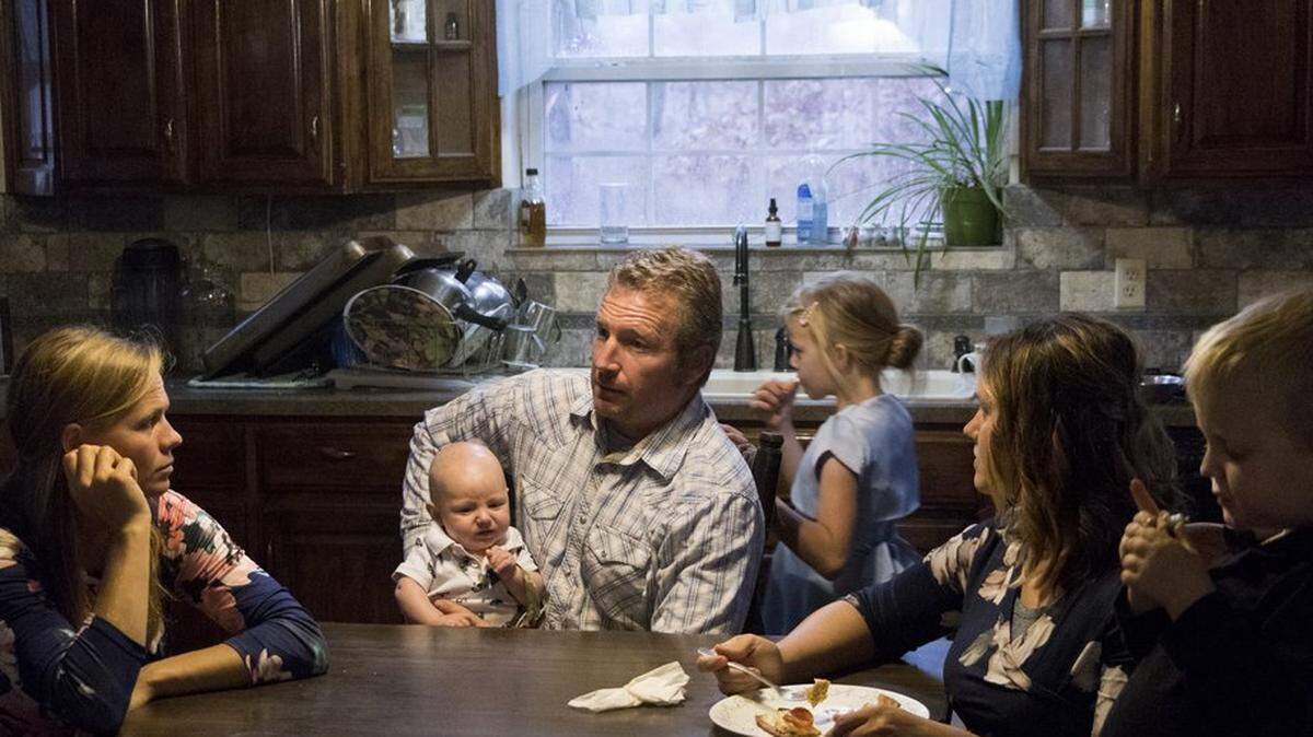 Flint Laub and his wives, Michelle Laub, left, and Ruth Anne Laub, are surrounded by some of their children in their kitchen at lunchtime on Nov. 18 on The Ranch near Humansville, Missouri. The family consists of 10 children, seven of which are Michelle’s and three of which are Ruth Anne’s. The family gathered together and ate pizza around the large wooden table in their kitchen after the morning’s church service.