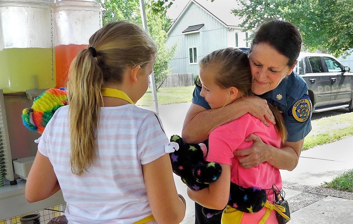 Leawood sisters Kaitlin Stotts (left) and Laurin Stotts wanted to do something to help the families of slain Wyandotte County sheriff's deputies Patrick Rohrer and Theresa King, so they decided to sell lemonade in their neighborhood. Maj. Kelli Bailiff with the Wyandotte County Sheriff's Office gave the girls a hug after thanking them and giving them teddy bears and other gifts.