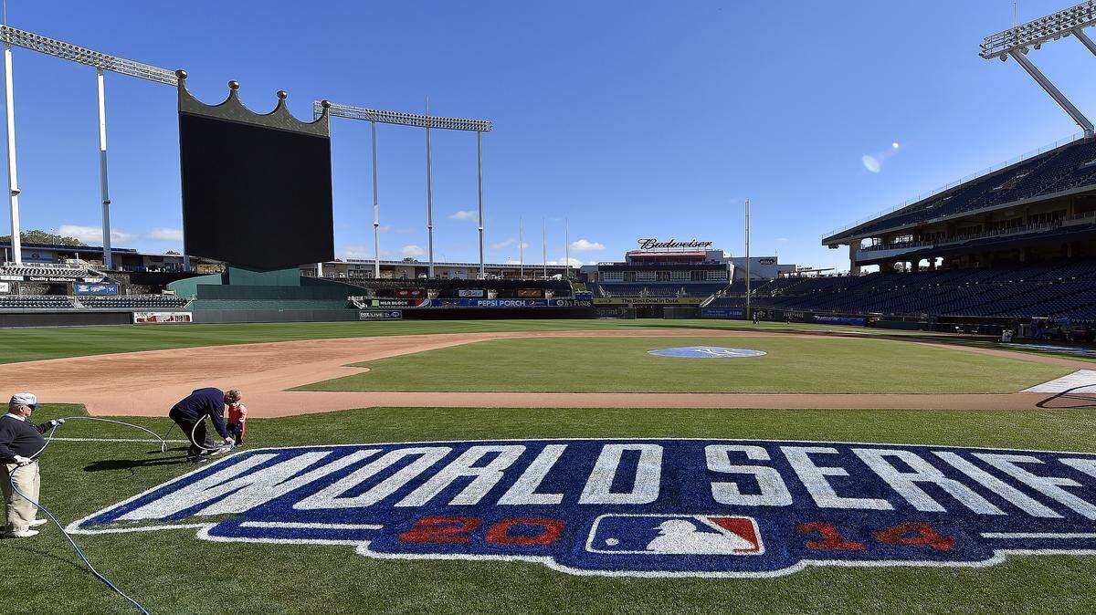 As George Toma holds the hose, Scott Parker puts the finishing touches on the 2014 World Series logo as his son, Andrew, 3, watches before Saturday's practice for the Royals at Kauffman Stadium.