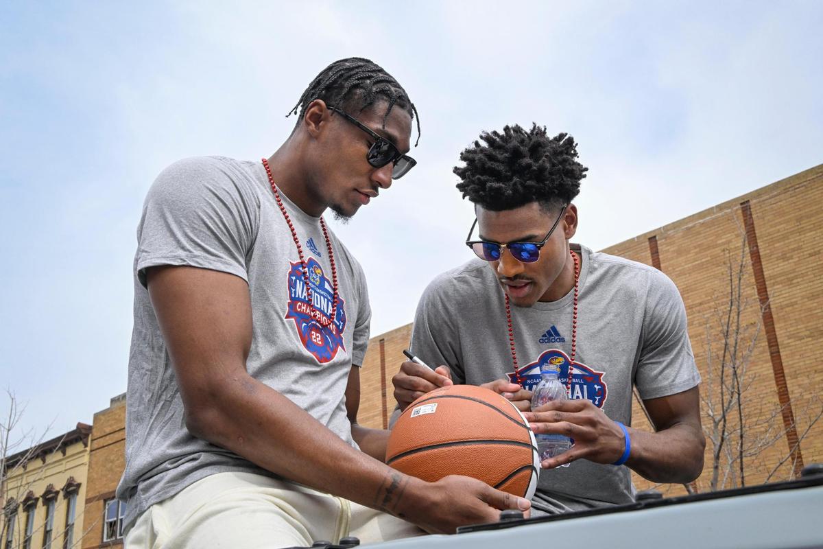 Ochai Agbaji, right, signs a fan’s basketball as teammate David McCormack holds it during the Jayhawks parade in Lawrence Sunday afternoon.