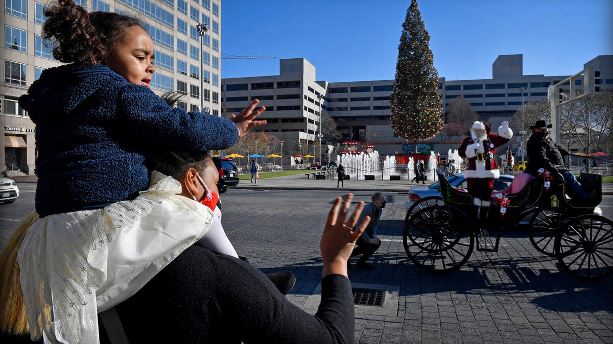Perched on her mother’s shoulders, Brooklyn Smith, 2, waves to Santa Claus, who made an appearance Friday morning to kick off the holiday season at Crown Center. Arriving in a horse-drawn carriage, Santa welcomed all the children before heading inside to his Gingerbread Station. Reservations can be made to visit with Santa from November 27 through December 24, 2020. Brooklyn and her mother, Sara Smith, are from Kansas City.