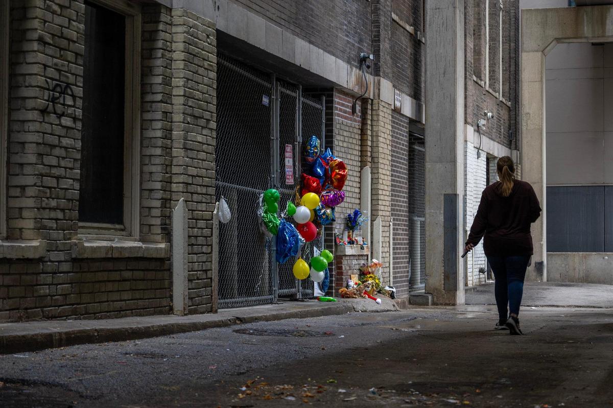 An unidentified woman walks past a makeshift memorial in an alley Friday near East 10th Street and Grand Boulevard in Kansas City. The memorial was set up for 5-year-old Grayson O’Connor who died after falling from a window of the Grand Boulevard Lofts on Nov. 27.