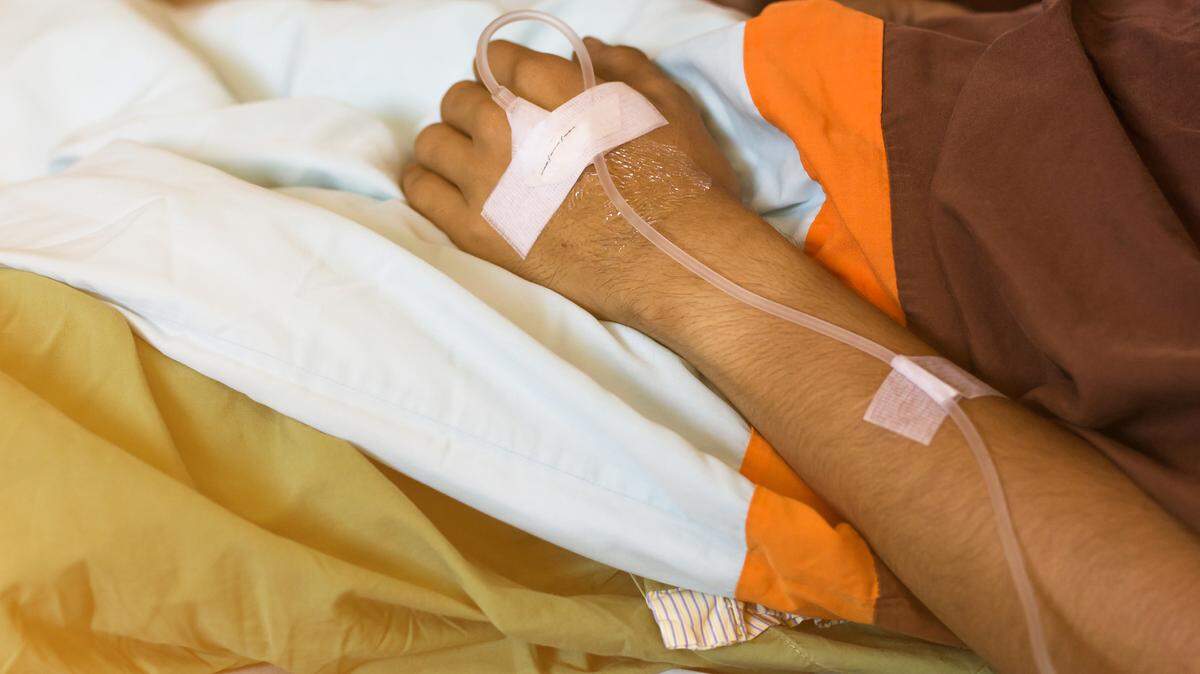 File photo of a man lying on a bed with an IV in his hand.