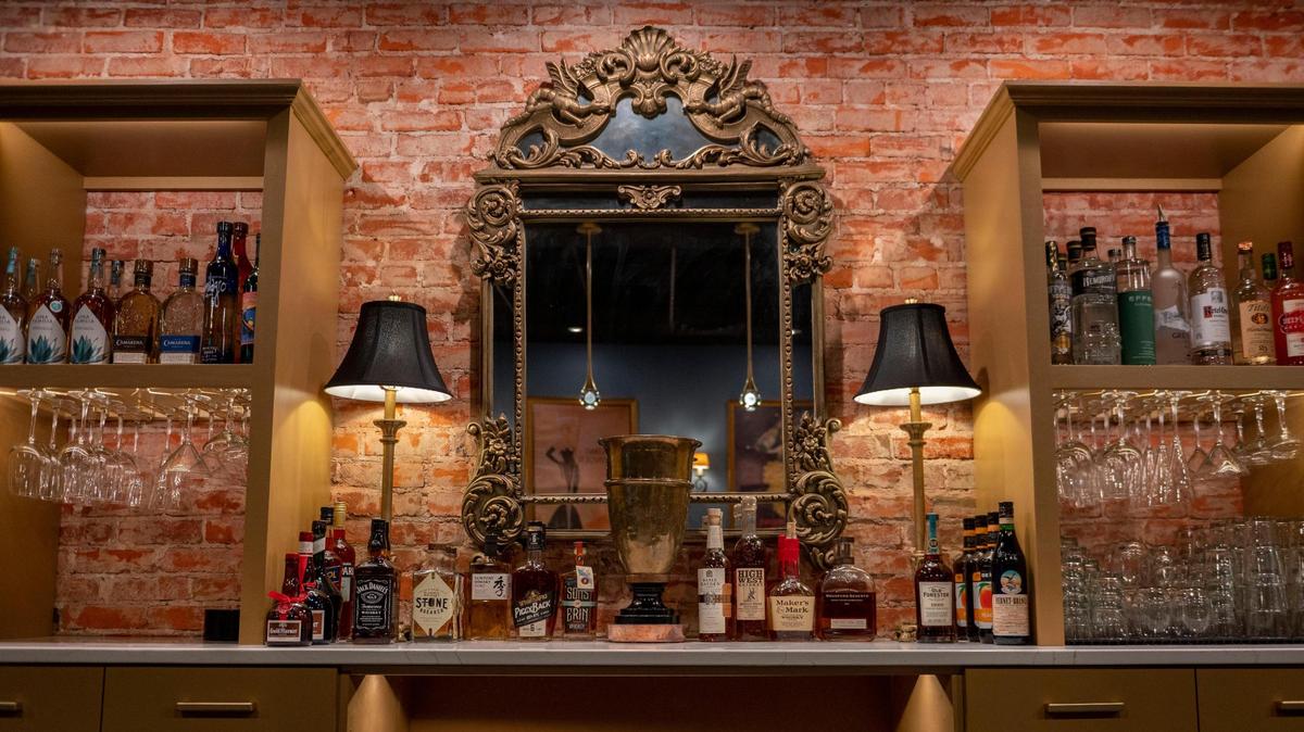 Liquor bottles and glassware are displayed on shelves next to a prominent brick wall at Uptown Lounge.