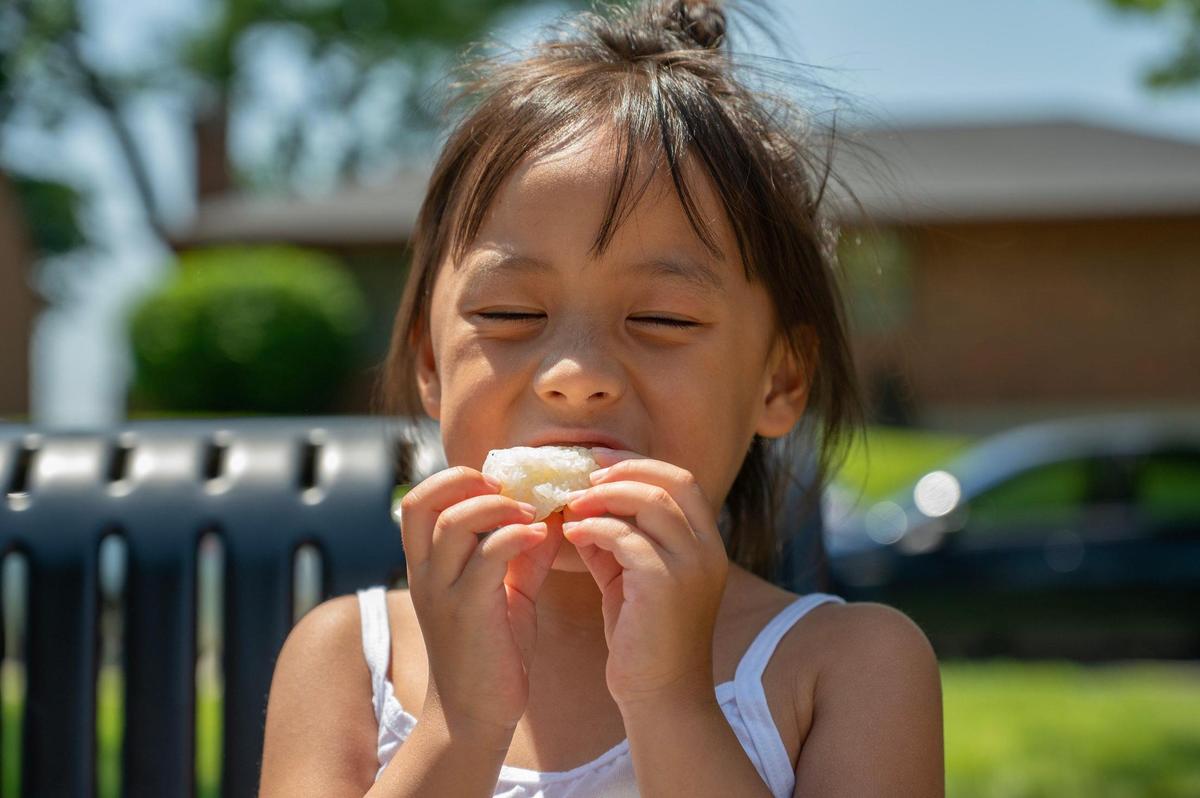 Four-year-old Estelle Cha enjoys a bowl of sticky rice from Laos House during the AAPIconic Festival on Saturday, May 20, 2023, in Kansas City.