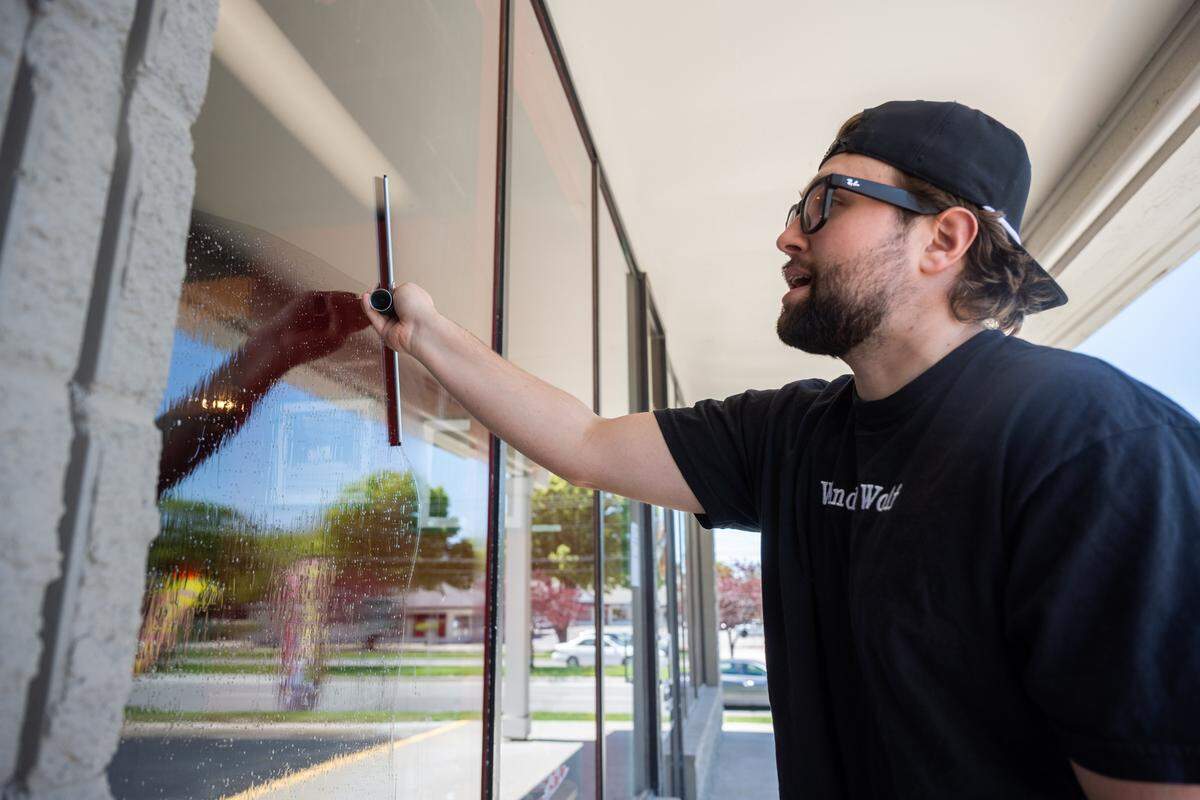 Davis Roethler cleans the front windows of Third Coast Pizza in Lenexa, on Monday, April 20, 2026. Roethler, whose company is named Window Wolf, uses social media to shine a light on small businesses and also cleans their windows for free.