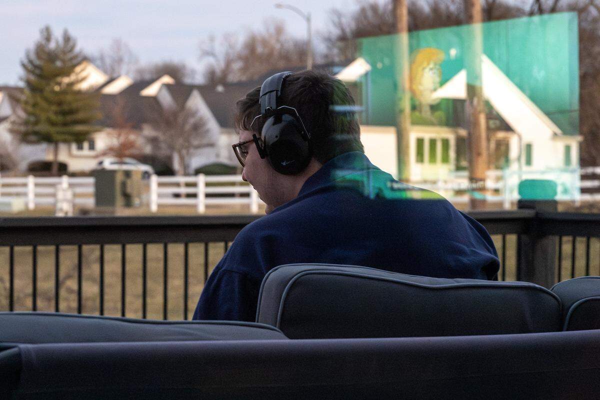 Harrison Long sits on a swing outside his home as Scooby-Doo plays on the TV, reflected in a window on Tuesday, Feb. 10, 2026, in Parkville.