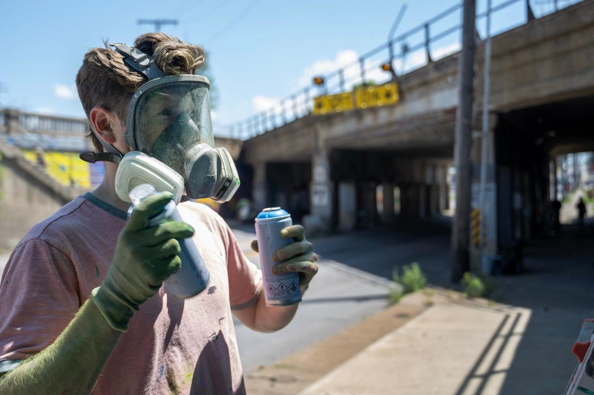 Artist Alex Eickhoff of Eye Cough Art shakes cans of aerosol paint for his mural on the Independence Avenue truck-eating bridge.
