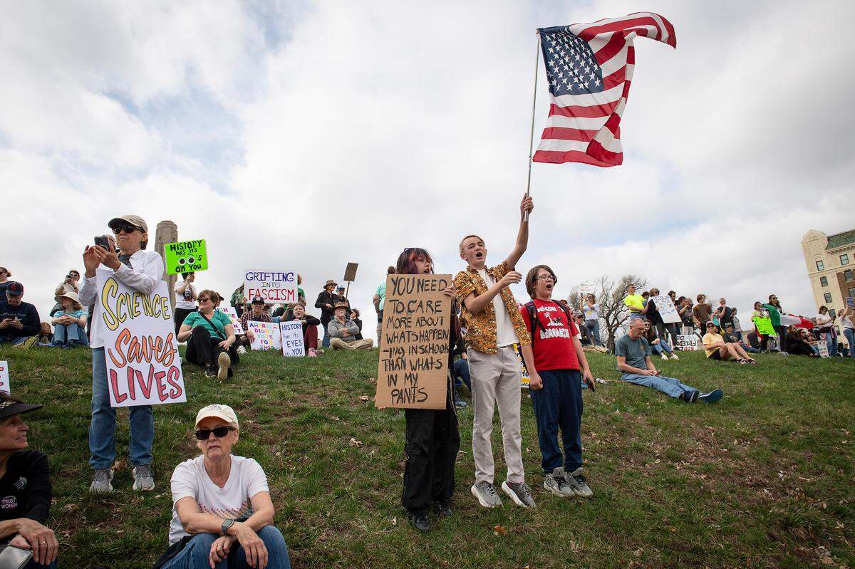 Isaac Fisher, 12, with flag, Kasper Sorio, 15, with sign, and Colin Grave, 12, shouted out protest chants during a pro-democracy rally that took aim at the Trump administration’s policies Saturday, March 29, 2025 in downtown Kansas City.