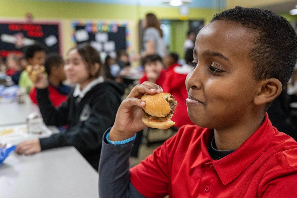 Zach Ibrahim, 10, a 5th grader at Scuola Vita Nuova Charter School, eats a cheeseburger made earlier in the day by Joe Joe’s Catering, part of the Westport Flea Market Bar & Grill which now serves some 5,000 school children around Kansas City.