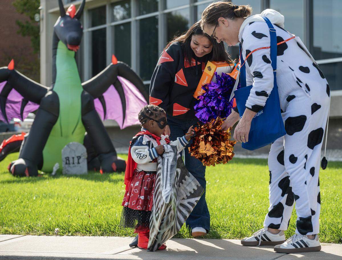 Two-year-old Penny Edwards, dressed in a costume, examines pom-poms held by Russell Stover employees as they hand out candy during the company’s annual Halloween giveaway at the headquarters on Friday, Oct. 31, 2025, in Kansas City.