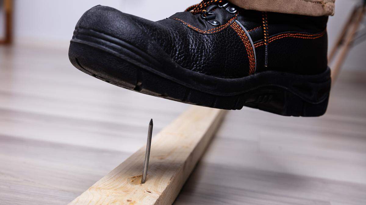 Close-up of man’s foot stepping over a nail inserted in wooden plank injury workman's compensation hurt workplace danger hazard